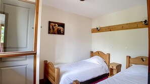 Une chambre à coucher avec deux lits en bois, une tête de lit en bois, une table de chevet, une étagère fixée au mur et un tableau représentant un ours.