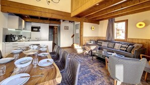 A spacious living area with a wooden ceiling, a dining table set for four, a sofa, and a patterned armchair. - 200m from ski slopes, 2nd floor, balcony, tv, 85m², Les Menuires (Les Menuires)