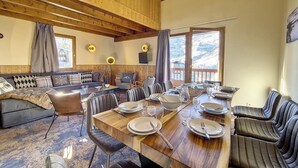 A dining area with a wooden table set for six, surrounded by leather chairs, with a view of a snowy mountain landscape through large windows. - 200m from ski slopes, 2nd floor, balcony, tv, 85m², Les Menuires (Les Menuires)