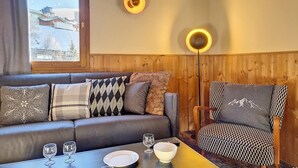 A cozy room with a wooden paneled wall, a leather sofa, a patterned armchair, and a table with glasses and a bowl. - 200m from ski slopes, 2nd floor, balcony, tv, 85m², Les Menuires (Les Menuires)