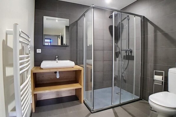 A modern bathroom with a glass-enclosed shower, a white sink, and a toilet.