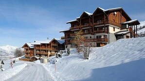 A multi-story wooden lodge with balconies, set against a snowy mountain backdrop. - 200m from ski slopes, Ground floor, balcony, tv, 90m², Les Menuires (Les Menuires)