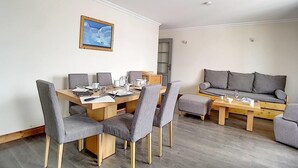 Un salon moderne avec une table à manger en bois, des chaises à revêtement gris, un canapé gris et un tableau encadré accroché au mur.