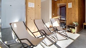 Una habitación con cuatro sillones reclinables, paredes de madera, una mesita con una planta y una puerta.