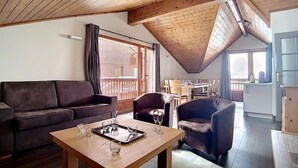 Un salon chaleureux avec un plafond en bois, un canapé, une table basse avec des verres et un coin repas avec des chaises.