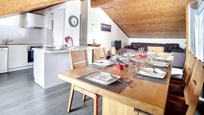 Une cuisine moderne avec des armoires blanches, un plafond en bois et un coin repas doté d’une table en bois, mise pour six personnes.