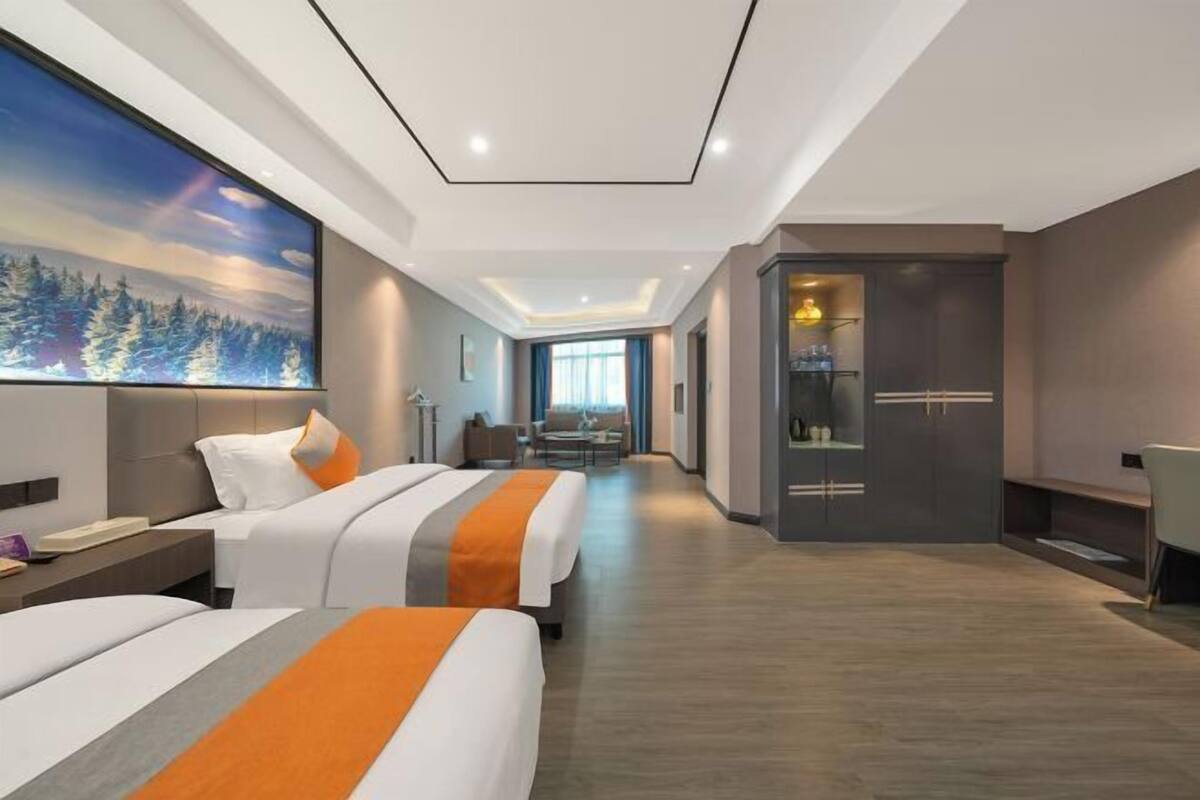 A modern hotel room with two beds, a large painting, a desk, and a view of the city.