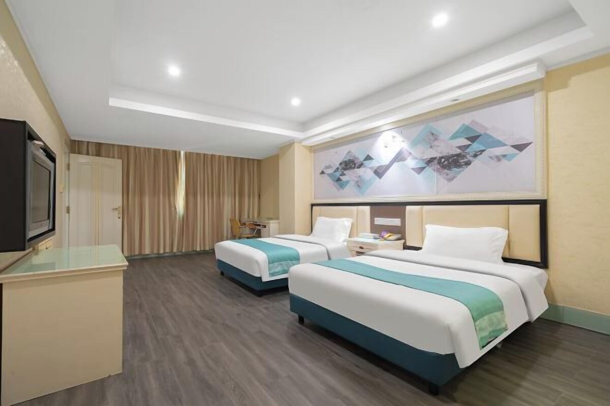 A hotel room with two beds, a TV, a desk, and a painting on the wall.