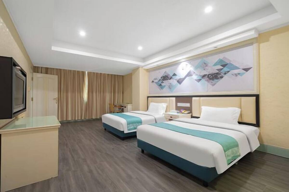 A hotel room with two beds, a TV, a desk, and a painting on the wall.