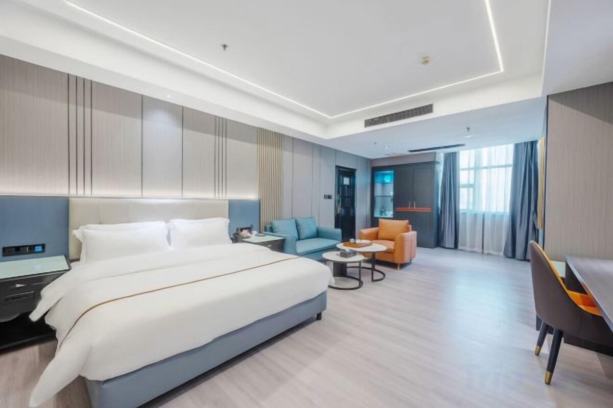 A modern hotel room with a large bed, a desk, a sofa, and a small table.