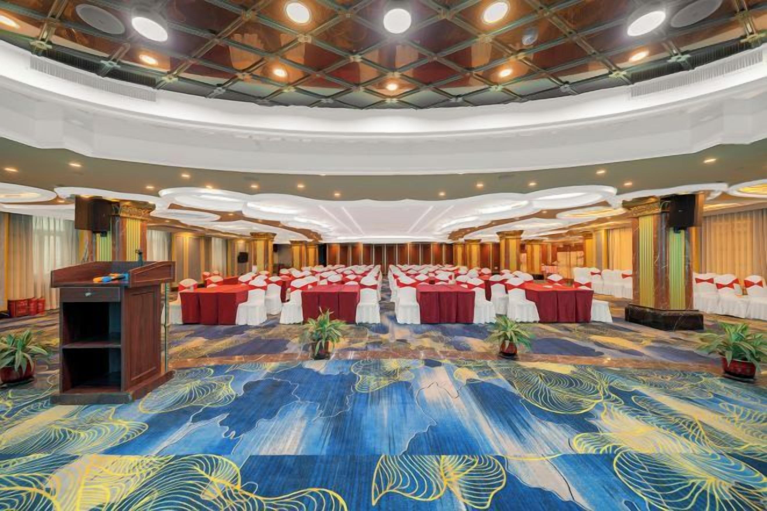Une grande salle de conférence avec un tapis bleu, plusieurs tables recouvertes de nappes rouges et un pupitre.
