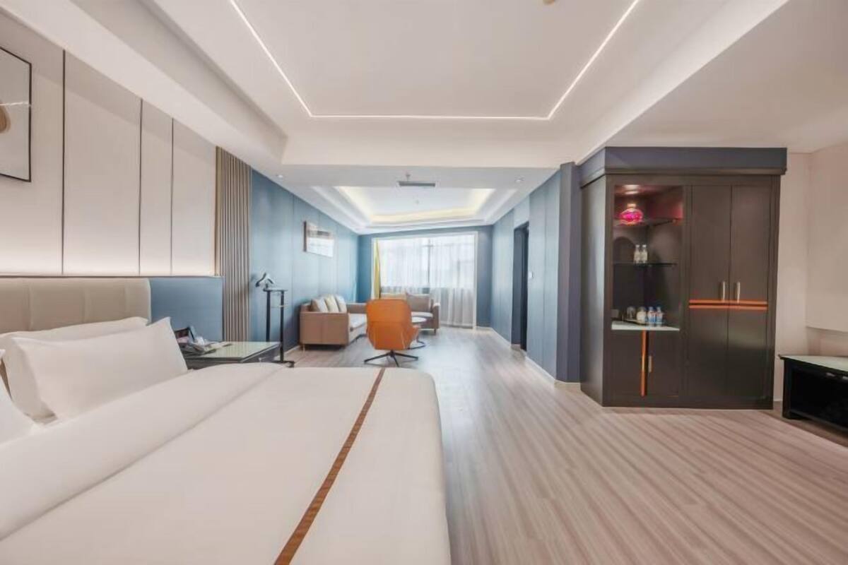 A modern hotel room with a large bed, a seating area with a sofa and chairs, a minibar, and a television.