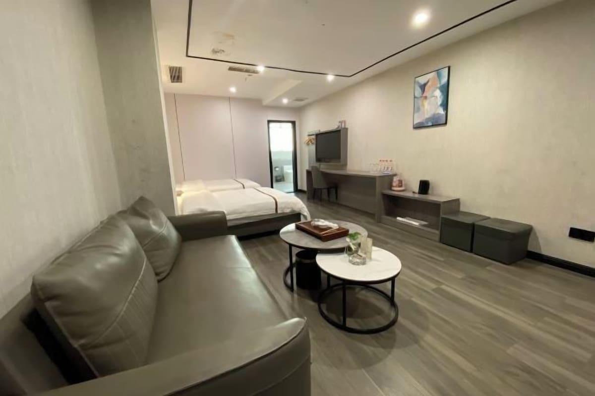 A modern hotel room with a sofa, a bed, a small round table, a TV, and a desk.
