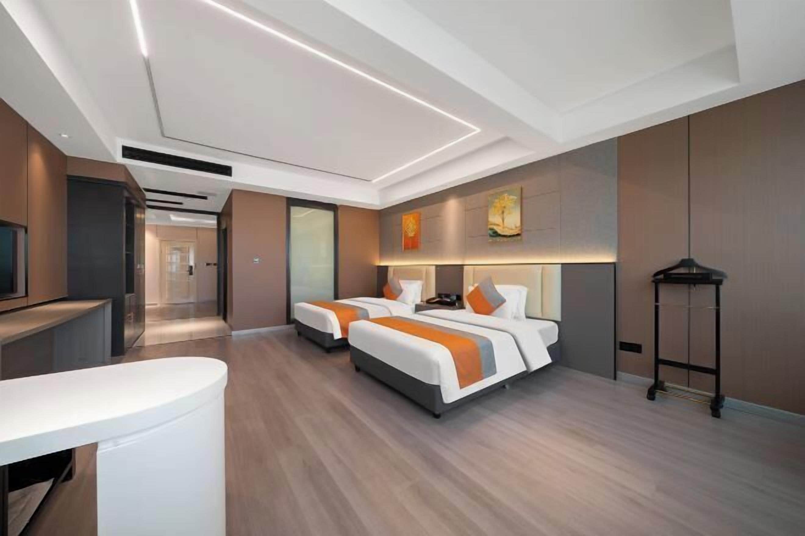 A modern hotel room with two beds, a desk, and a TV.