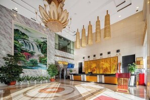 A hotel lobby with a reception desk, a large mural, potted plants, and a chandelier. - Hao Fu Hua Hotel (Quanzhou)