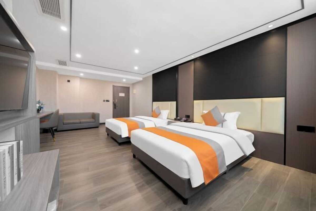 A modern hotel room with two beds, a sofa, and a TV.