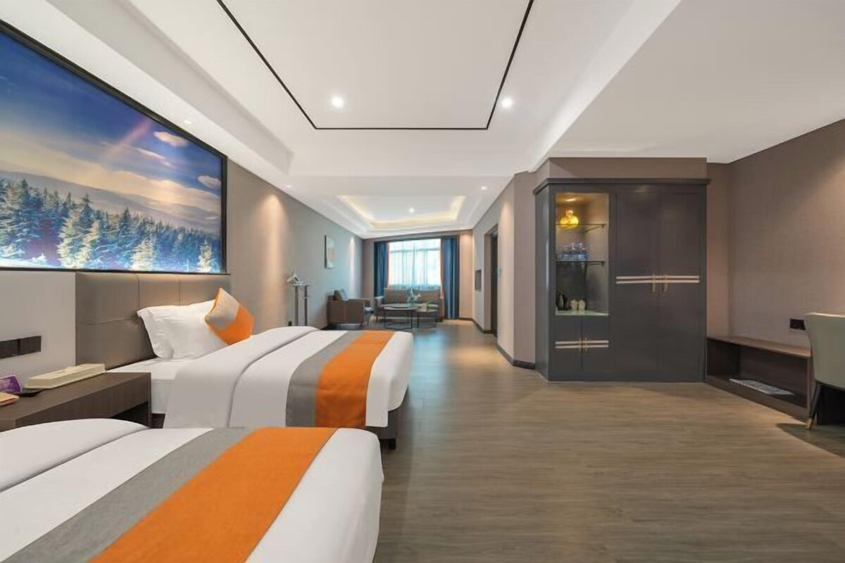 A modern hotel room with two beds, a large painting, a desk, and a view of the city.