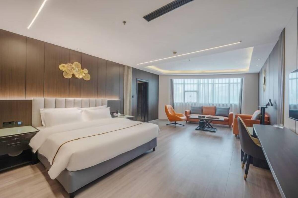 A modern hotel room with a large bed, a desk, and a sofa.