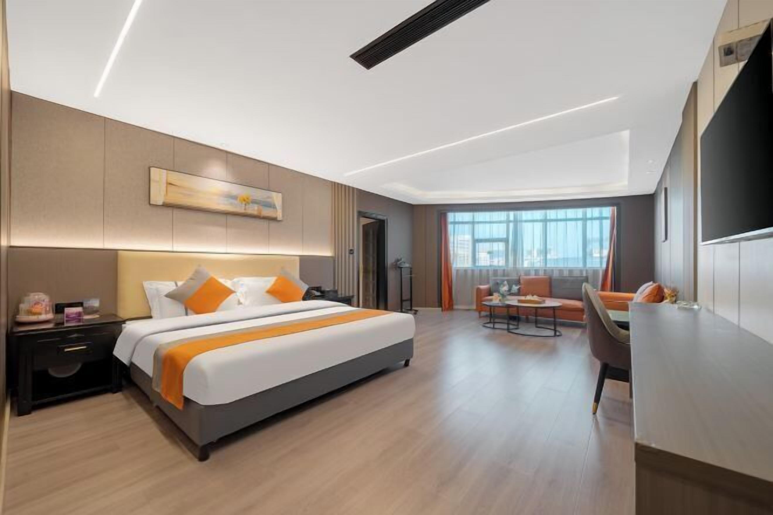 A modern hotel room with a large bed, a desk, a chair, and a view of the city.