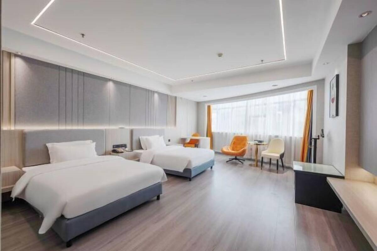 A modern hotel room with two beds, a desk, a chair, and a large window.