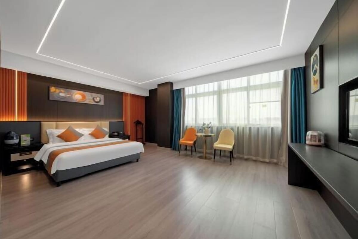 A modern hotel room with a bed, a desk, two chairs, and a large window.