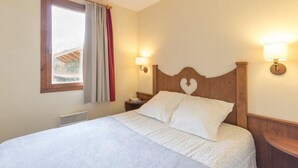 A bedroom with a wooden headboard, two bedside lamps, a window with curtains, and a radiator. - 100m from shops, 1st floor, view street, 32m², Serre Chevalier (SERRE CHEVALIER)