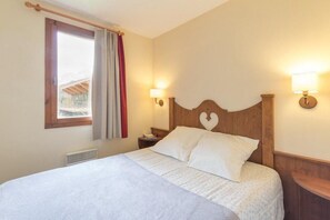 A bedroom with a wooden headboard, two bedside lamps, a window with curtains, and a bed with white bedding.