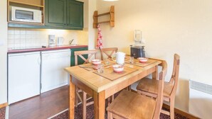 A compact kitchen with a wooden table, chairs, a microwave, a coffee maker, and a kettle. - 100m from shops, 1st floor, view street, 32m², Serre Chevalier (SERRE CHEVALIER)