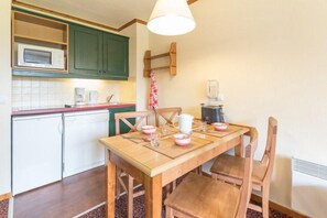 A compact kitchen with a wooden table, chairs, a microwave, a coffee maker, and a kettle.