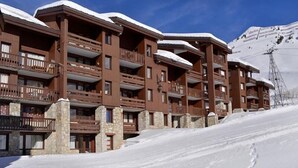 Een meerlaags hotel met balkons, stenen pilaren en een besneeuwde berg op de achtergrond.