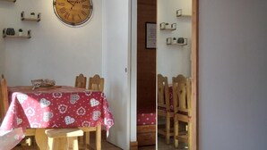 Een eetgedeelte met een houten tafel en stoelen, een wandklok en planken met kleine planten.