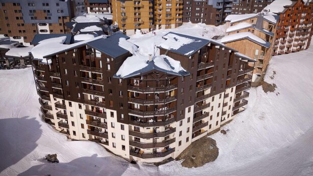 A multi-story hotel with balconies and a snow-covered roof, surrounded by other buildings. - 150m from ski slopes, Ground floor, balcony, 30m², Val Thorens (Val Thorens)
