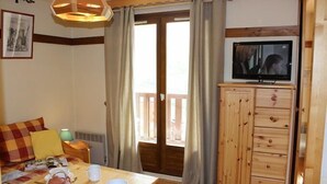 A cozy room with a wooden table, a television, and a sliding door to a balcony. - 150m from ski slopes, Ground floor, balcony, 30m², Val Thorens (Val Thorens)