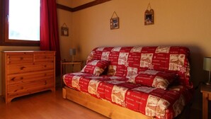 A bedroom with a wooden dresser, a bed with a red and white patterned bedspread, a window with red curtains, and a wooden ceiling beam. - 150m from ski slopes, Ground floor, balcony, 30m², Val Thorens (Val Thorens)