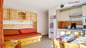 Ein kleines Zimmer mit einem Holzbett, einem Tisch und einer Küchenzeile.