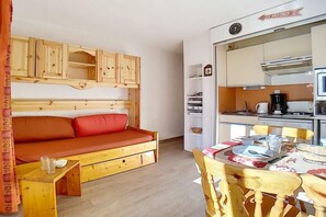 Una habitación pequeña con una cama de madera, una mesita y una kitchenette.