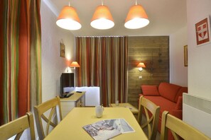 Una habitación con escritorio de madera, sillas, cama con ropa de cama roja, televisor y cortinas a rayas.