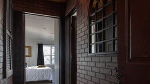 Een houten gang die leidt naar een slaapkamer met een bed, een raam en een deur.