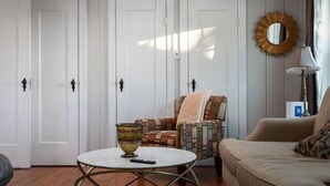 Een kamer met een ronde tafel, een gestreept fauteuil, een bank en een spiegel aan de muur.
