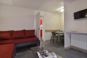 Um espaço compacto com sofá vermelho, mesa de jantar com cadeiras e uma TV de tela plana na parede.