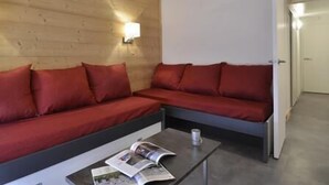 Ett modernt rum med en sänggavel i trä, en röd soffa och ett litet bord med en tidning på.