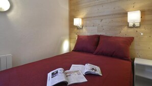 Ett sovrum med en sänggavel i trä, två sänglampor, ett rött överkast och en tidning på sängen.