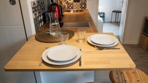 Una pequeña cocina con una mesa de madera preparada para dos personas, un hervidor rojo y un salpicadero decorativo.