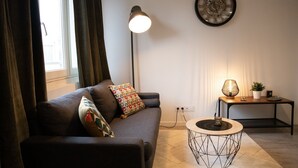 Una sala de estar con un sofá, una lámpara, un reloj y una pequeña mesa con una planta.