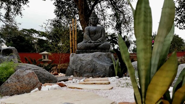 A serene garden with a large Buddha statue, surrounded by rocks and plants. - Your Personal Paradise in ZenGarden: Cozy Vacation Home for Couples in Paraguay (Ñemby)