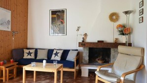 A cozy living room with a blue sofa, a wooden coffee table, a beige armchair, and a fireplace. - 3rd floor, view village, balcony, fireplace or stove, tv, 49m², Le Grand Bornand (Le Grand-Bornand)