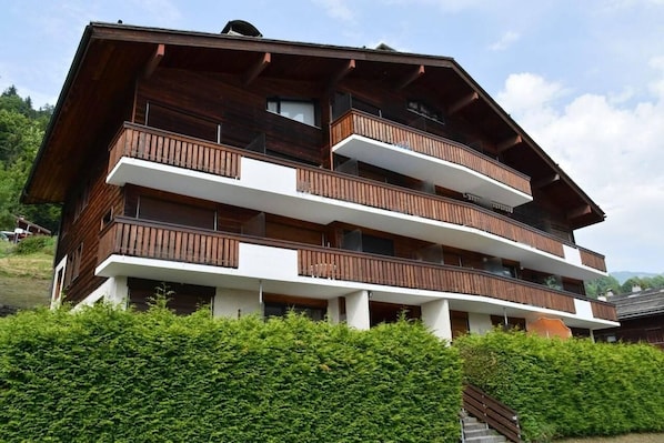 A multi-story wooden building with balconies, surrounded by greenery.