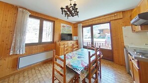 Eine Holzhütte mit Esstisch, Stühlen, einer Chandelierleuchtre, einer Küchenzeile und großen Fenstern.