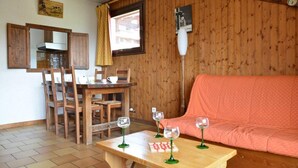 Ein gemütliches Zimmer mit Holzvertäfelung, einem Esstisch mit Stühlen, einer Couch und drei Weingläsern auf einem kleinen Tisch.