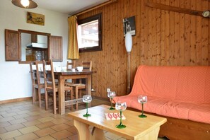 A cozy room with a wooden interior, a dining table with chairs, a sofa, and three wine glasses on a small table.